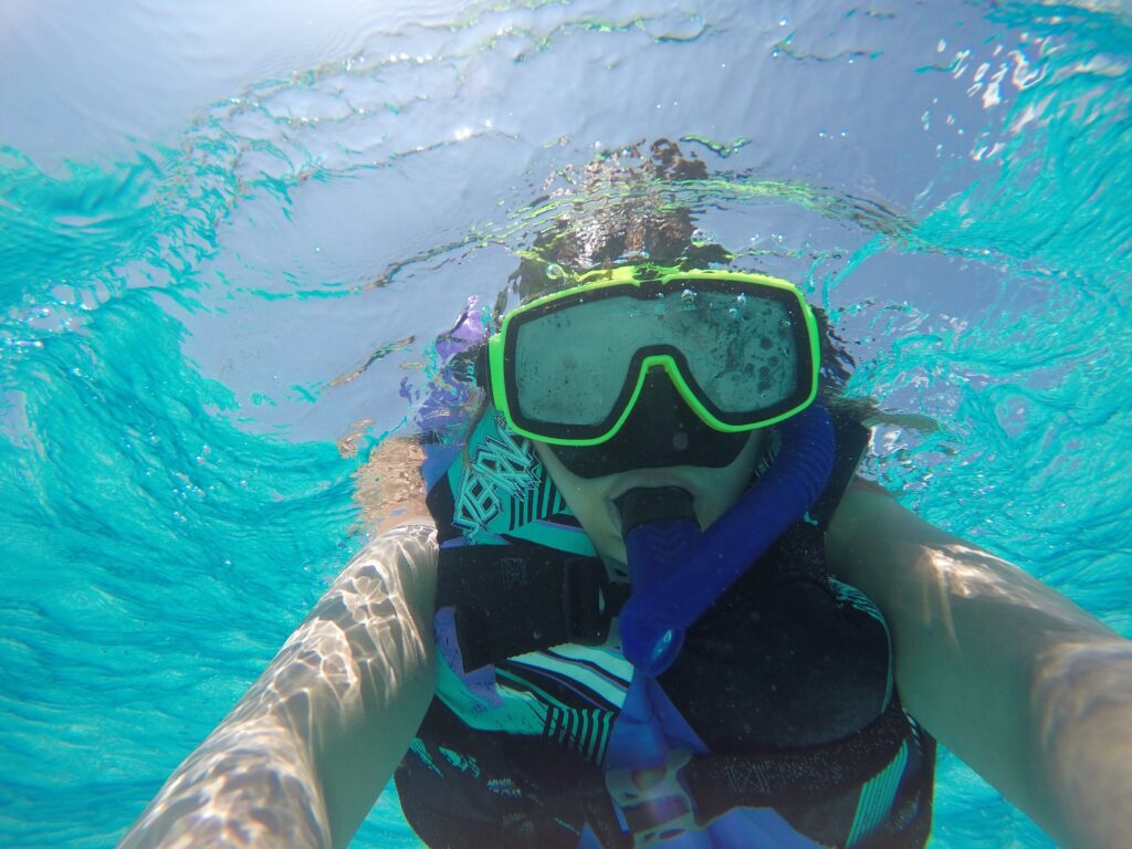 Close-up of a snorkeler wearing a mask, snorkel, and flotation vest in clear turquoise water