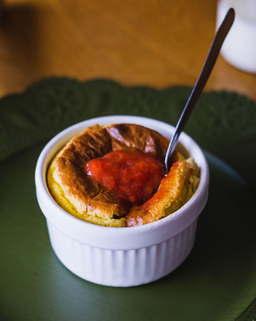 Golden-topped soufflé in a white ramekin with red fruit sauce, served at Cafe Jacqueline North Beach, San Francisco