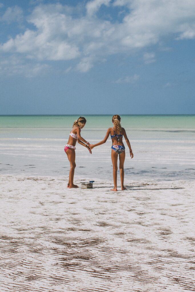 Two girls playing on the vast shallow white sand beach of Holbox Island with turquoise Caribbean water in the background, Quintana Roo, Mexico