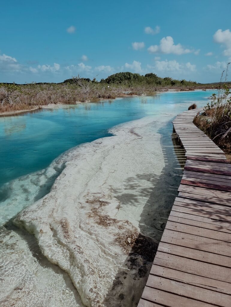 Wooden boardwalk path alongside shallow crystal clear turquoise lagoon water surrounded by mangrove wetlands on Holbox Island, Quintana Roo, Mexico