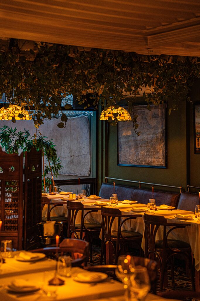 Dimly lit French restaurant dining room with candlelit tables, white tablecloths, and warm lamplight, evoking the cozy atmosphere of Cafe Jacqueline in San Francisco