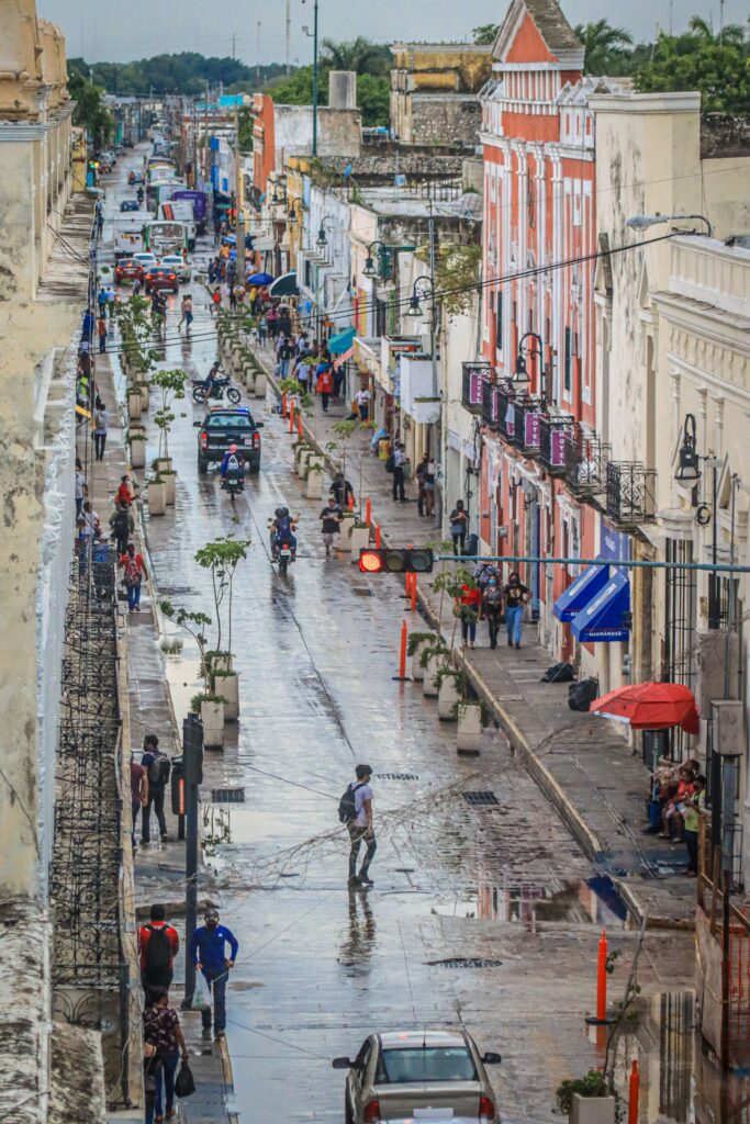 Aerial view of a rainy downtown street in Mérida, Mexico with colorful colonial buildings and locals walking