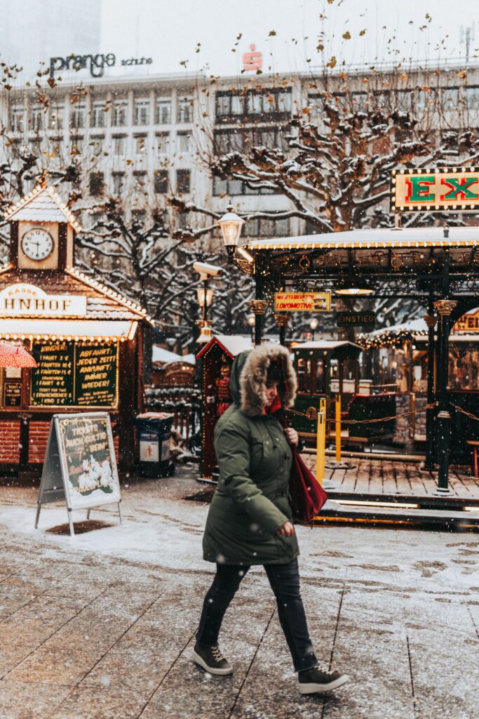 A woman walking through a snowy German Christmas market in Munich Germany with illuminated wooden stalls warm lights and snow-covered trees in winter