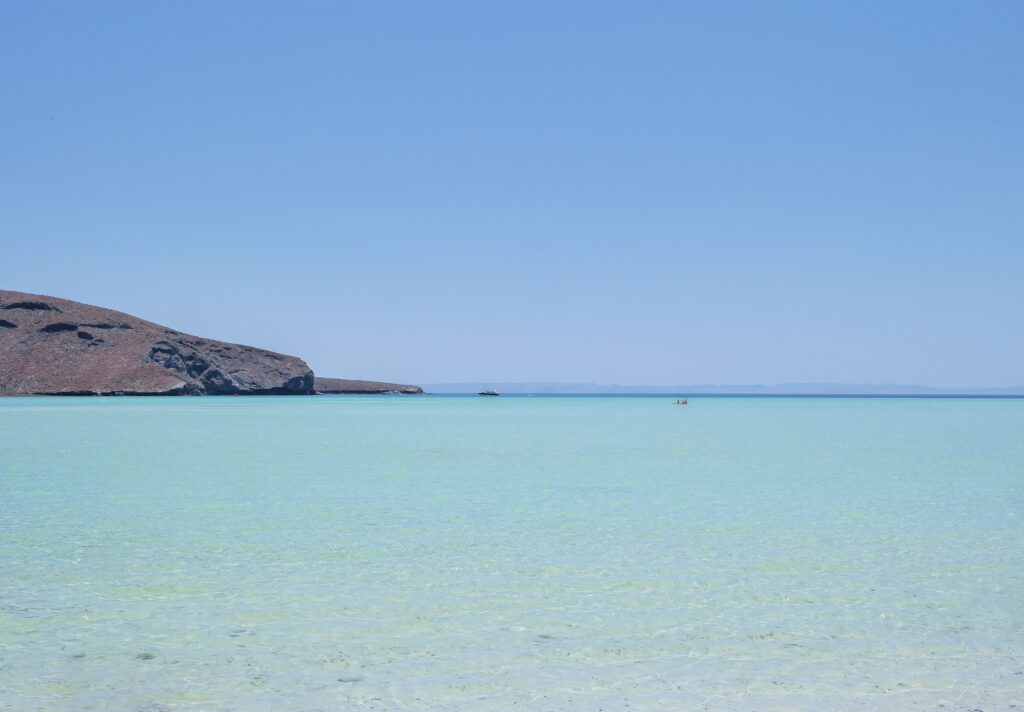 Wide panoramic view of Playa Balandra's crystal clear pale turquoise lagoon with dry desert rocky hills and deep blue sky near La Paz, Baja California Sur, Mexico