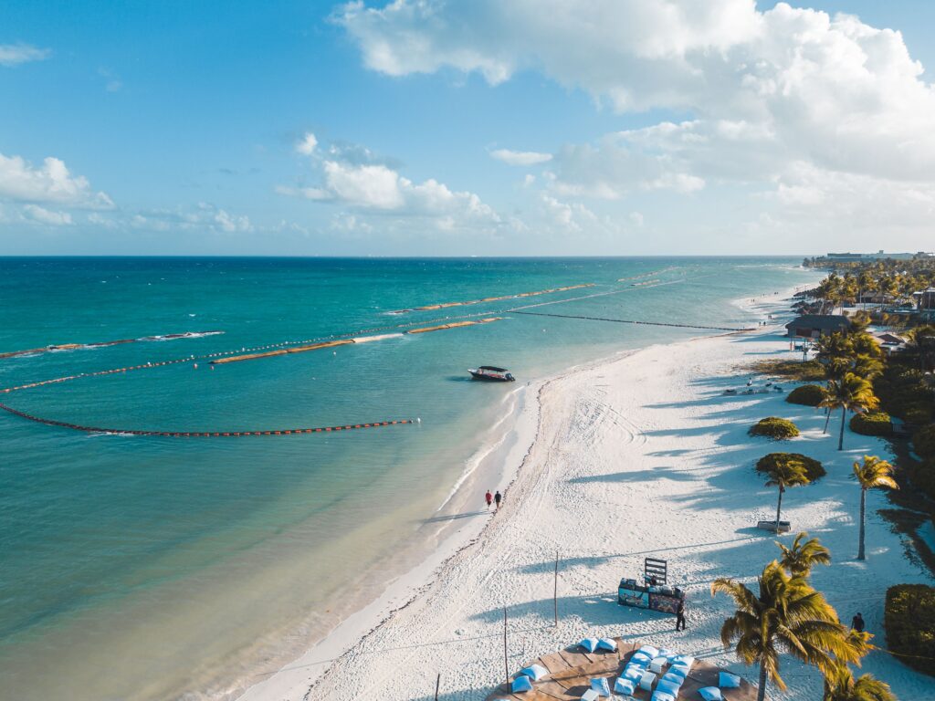 Aerial view of Playa Norte on Isla Mujeres showing calm shallow turquoise Caribbean water, powdery white sand beach lined with palm trees and beach clubs in Quintana Roo, Mexico