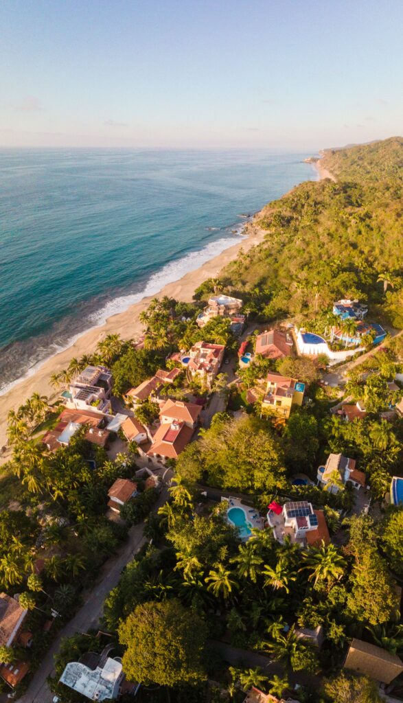 Aerial drone view of Sayulita bohemian village with colorful terracotta villas nestled in tropical jungle hillside beside the Pacific Ocean beach in Nayarit, Mexico at golden hour