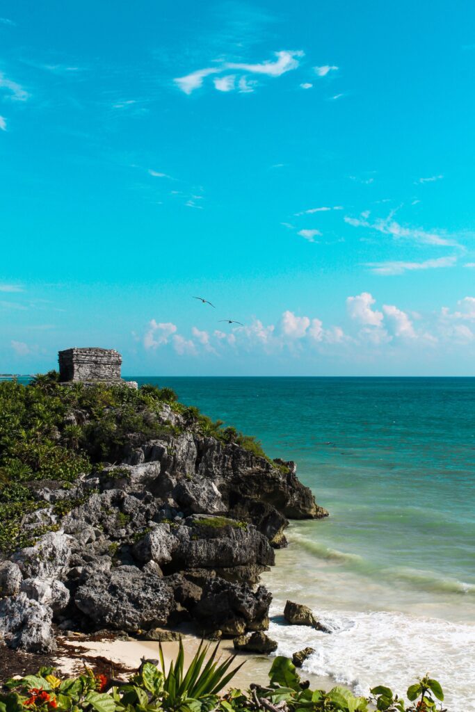 Ancient Mayan temple ruins perched on a rocky cliff above a white sand beach with turquoise Caribbean water in Tulum, Quintana Roo, Mexico